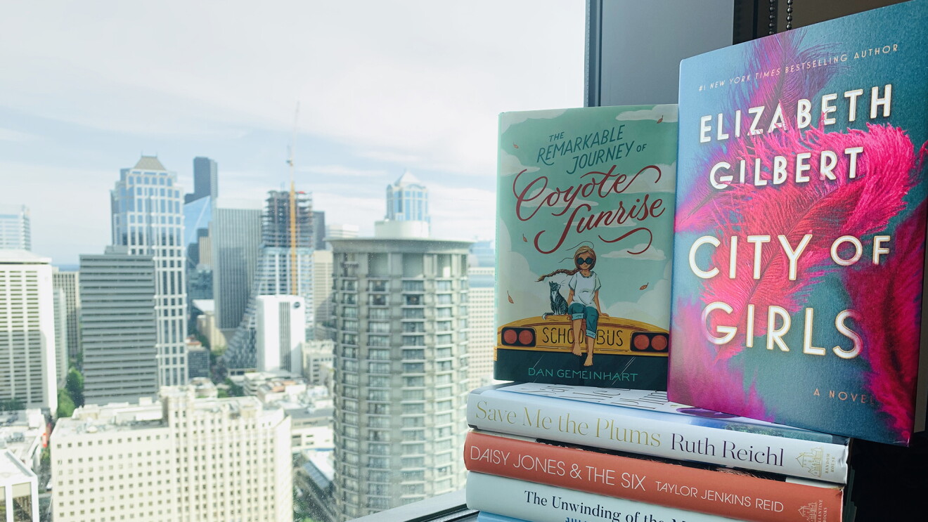 Stack of books in the window overlooking skyscrapers in Seattle. Books are among the "Best books of the year" for 2019.