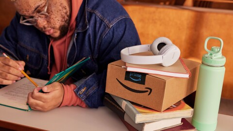 Un étudiant étudie à son bureau avec un colis amazon, des écouteurs et une bouteille d'eau.