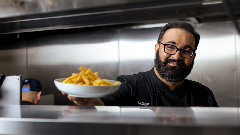 A photo of Nomie Hamid, chef and owner of Virtual X Kitchen, holding a plate of french fries.