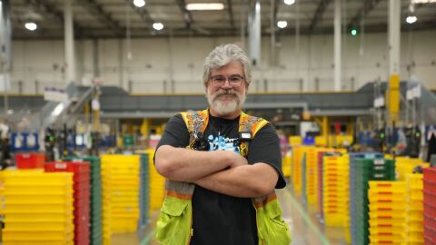 cheerful employee wearing safety vest stands confidently among yellow storage bins