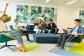 Parte del equipo que prepara el Prime Day se encuentra en una sala de las oficinas corporativas viendo cómo evoluciona el día. Tres de ellos están sentados en el sofá y tres más en sillones. Todos ellos tienen los ordenadores sobre las piernas. Los colores de las paredes y del suelo son amarillos y verdes y azules. 