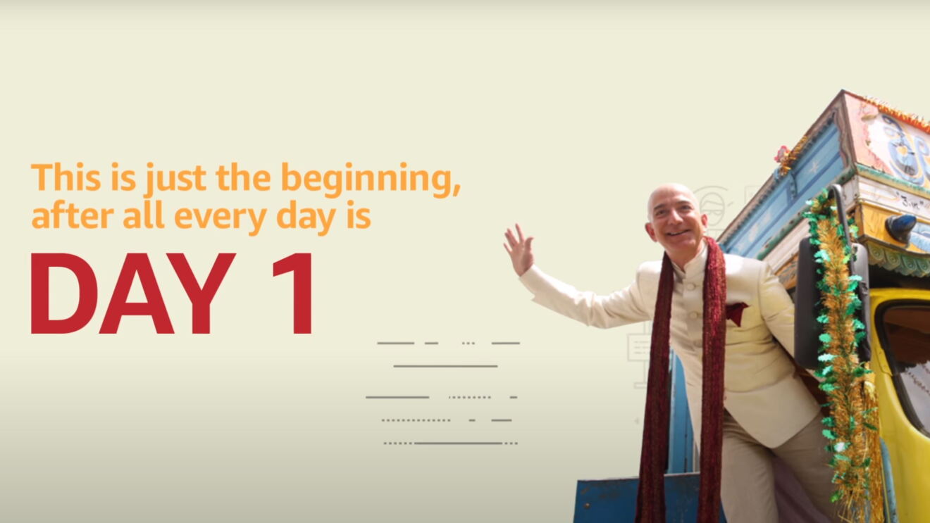 A composite image that shows Jeff Bezos leaning out of, and waving from, a rickshaw. To the left, text overlay says " This is just the beginning, after all, everyday is day 1."