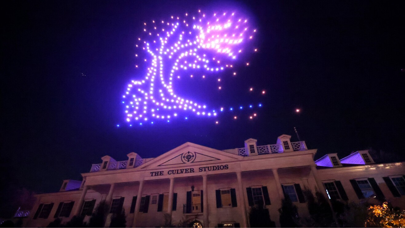 Glowing purple lights in the night sky show a tree. Below the light display is the Culver City Studios building.