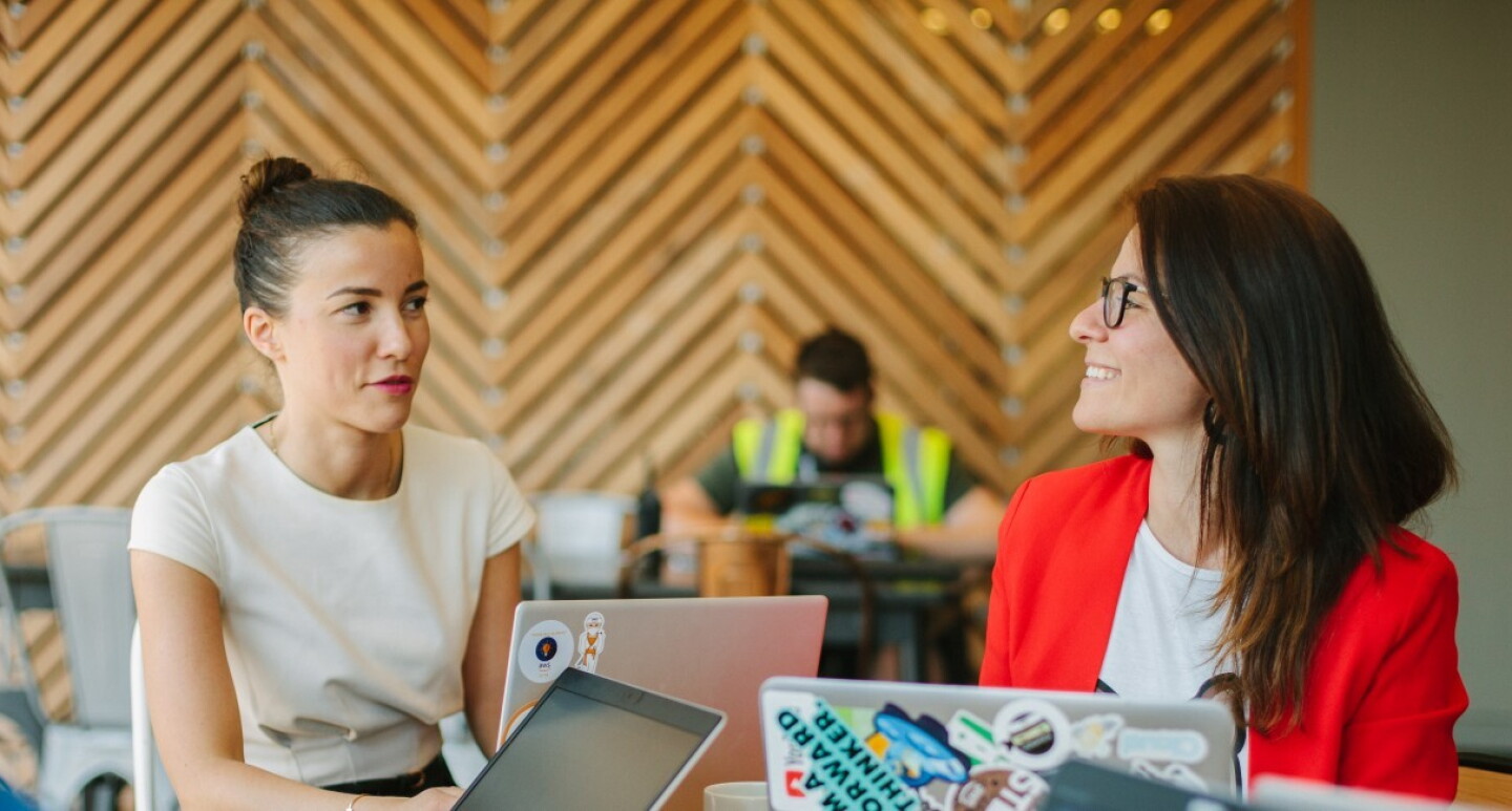 Drei Frauen sitzen am Schreibtisch, arbeiten zusammen und sprechen miteinander