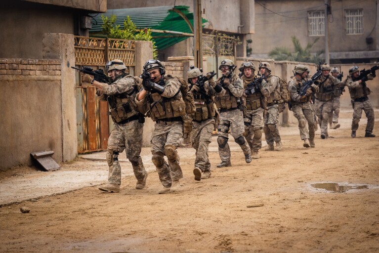 A still from Warfare, showing a military platoon cautiously progressing through a desert street while holding weapons