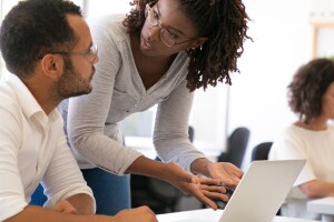 A photo of two students conversing in front of a laptop device. 