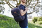 A man stands in a grassy field with a blue Hipcub backpack.