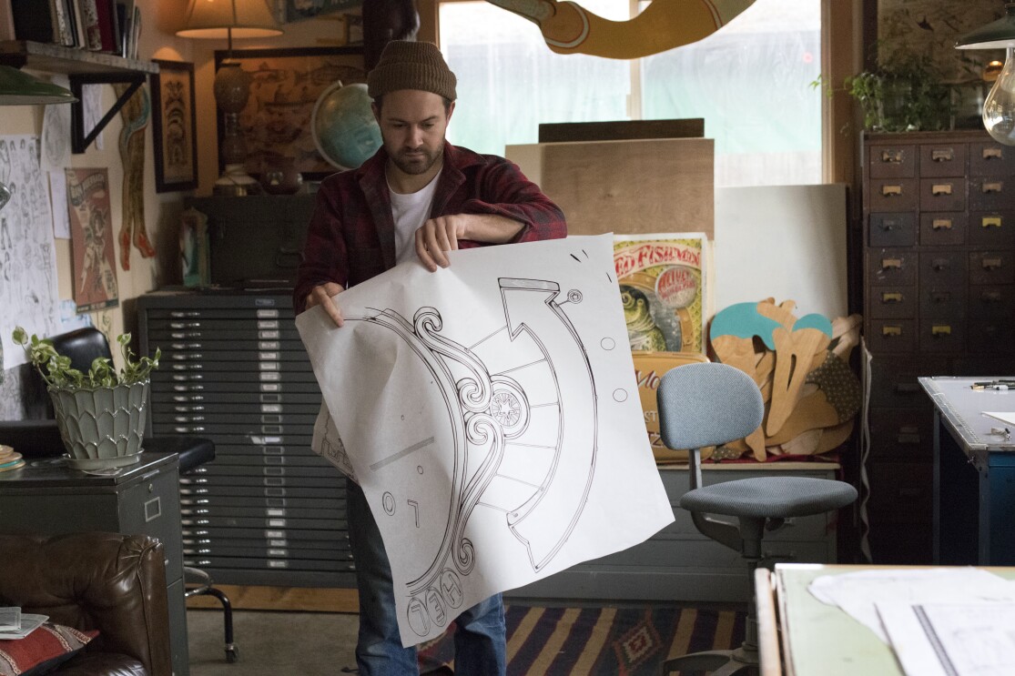 Amazon artist Kyler Martz in his Seattle studio holding a drawing of an upward pointing arrow.