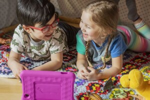 An image of two kids playing on the floor looking at an Amazon Kids tablet. 