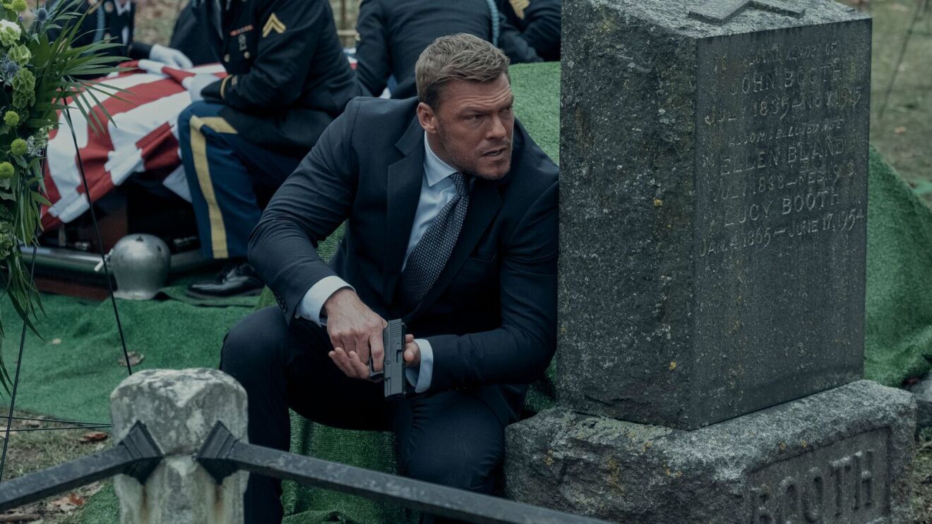 jack reacher crouched behind a tombstone holding a gun in the prime video series reacher