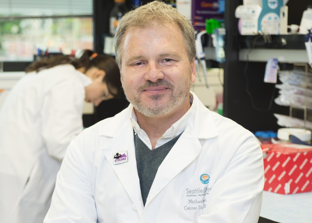 An image of Dr. Jensen, a childhood cancer researcher and physicians from Seattle Children's Hospital. He is wearing his white coat and smiling for a head shot photo.