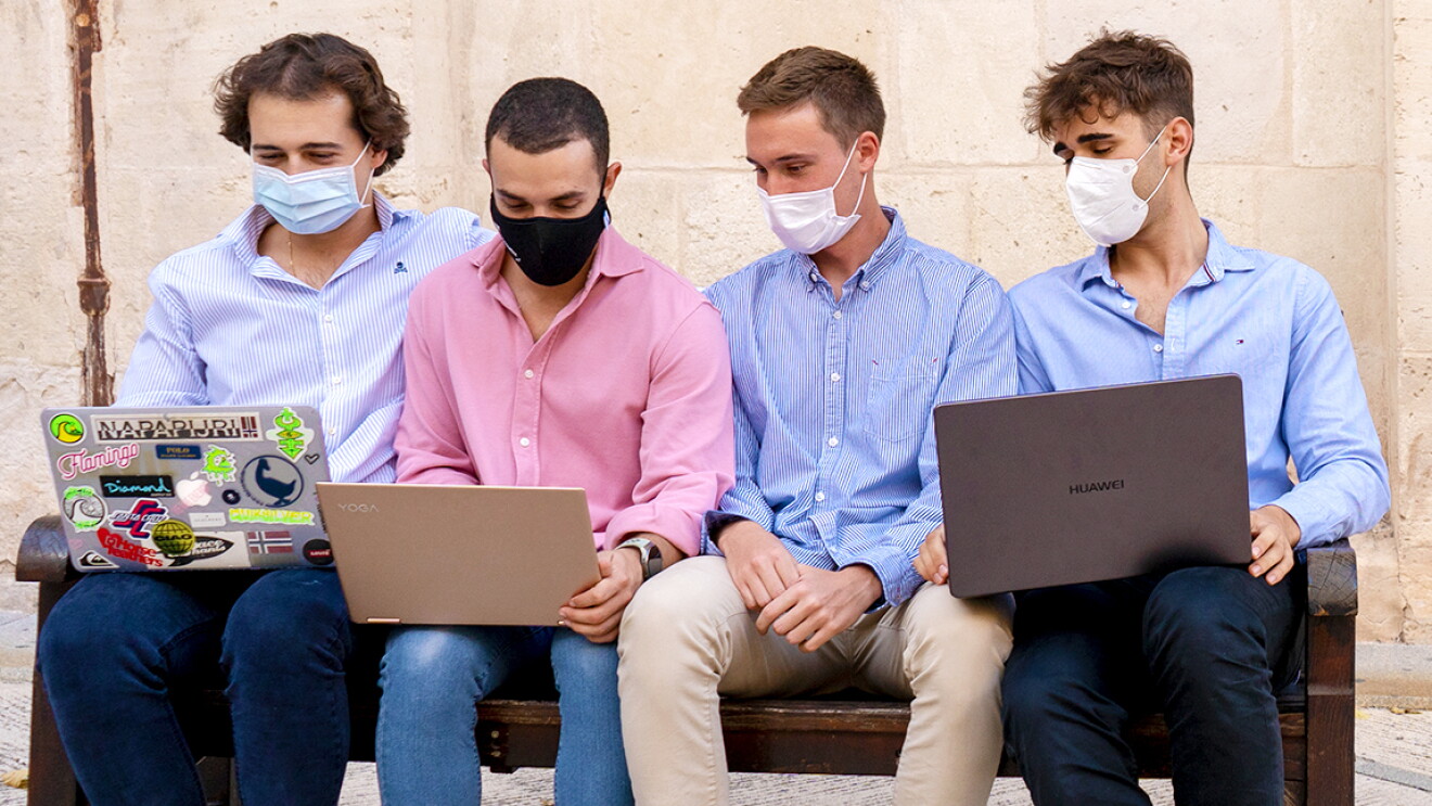 Javier Olivares, Jordi Cascant, Eloy Ribera y Iván Arenas forman EasyVal, el equipo ganador de la primera edición de Amazon Campus Challenge. Los cuatro están sentados en un banco de madera en la calle con un fondo de pared de piedra, Todos menos Eloy tienen un ordenador en las piernas. Javier va con jeans y camisa de rayas, un collar de oro y el pelo marrón y por la oreja. Su ordenador está lleno de pegatinas. Su mascarilla es quirúrgica. Jordi tiene una camisa rosa y jeans. Tiene un reloj en la mano izquierda y una mascarilla negra. Eloy no tiene ordenador, lleva una camisa azul de rayas y es´ta mirando el ordenador de Jordi. Iván también con mascarilla, camisa azul y un ordenador en las piernas. 