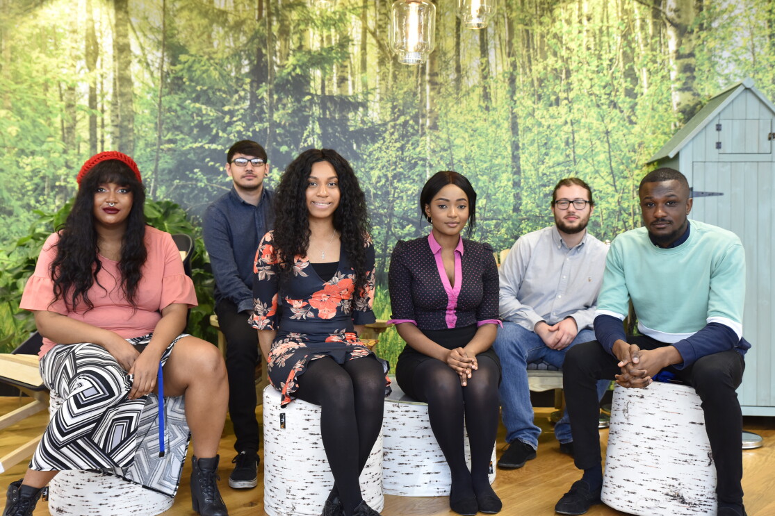 AWS Graduates sitting near each other in front of a forst wallpaper.