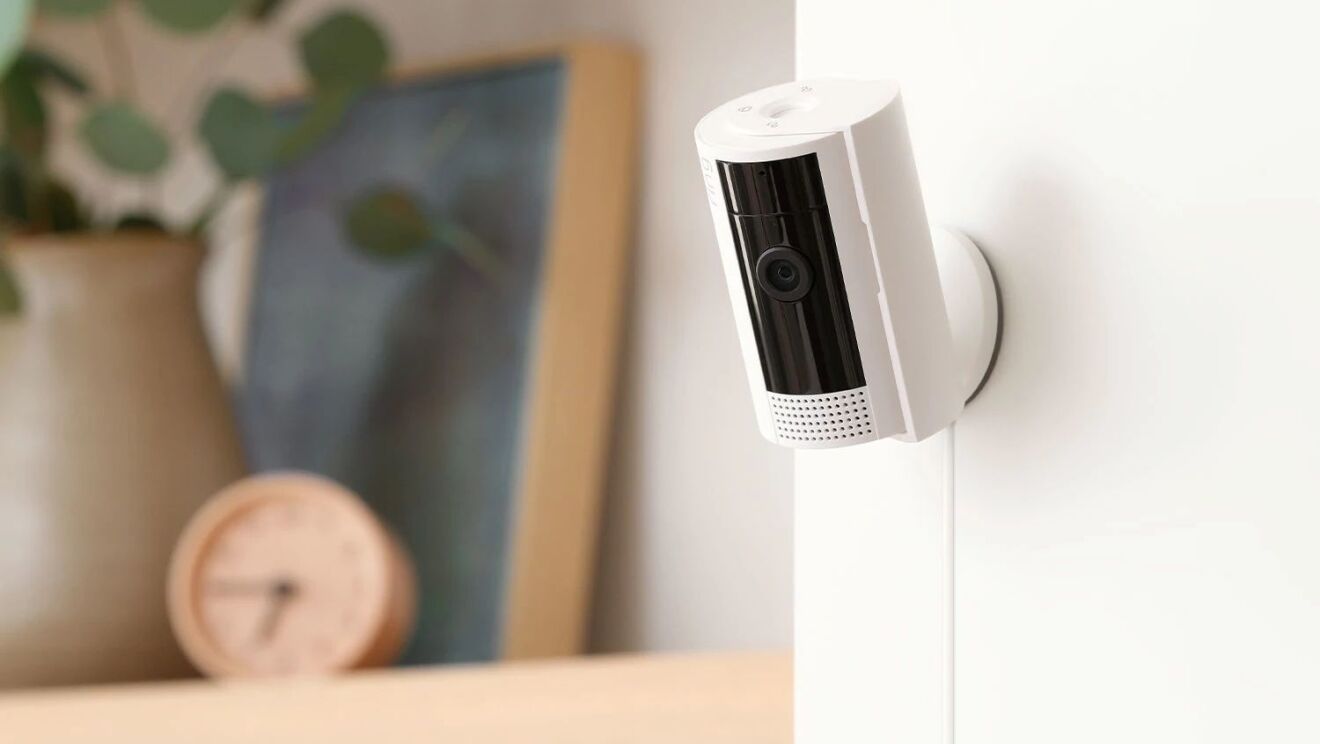 本棚の横の壁に取り付けられている白い円筒形のセキュリティカメラ。Amazon Ring