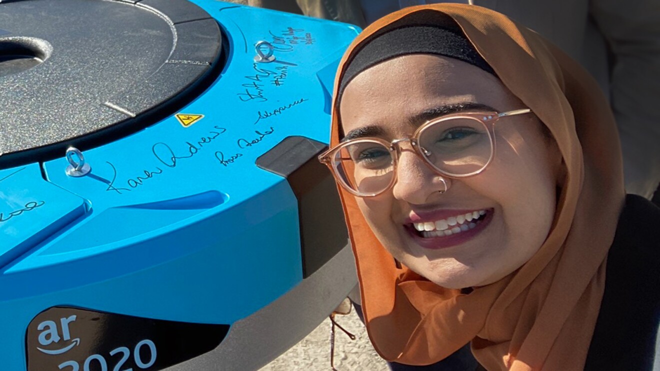 A woman poses with an Amazon Robotics unit.