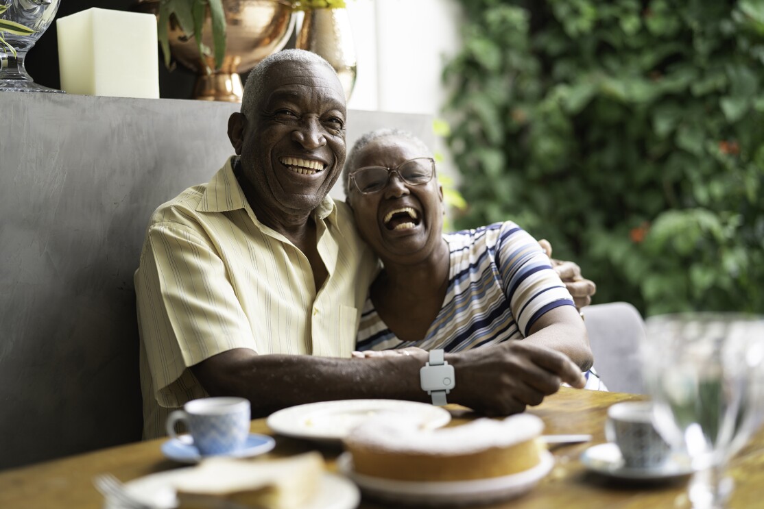 An image of a senior couple sitting in a booth at a table hugging each other and smiling.