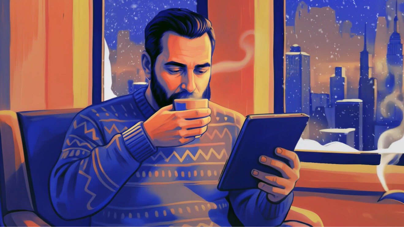 Man in patterned sweater sips coffee while using tablet, city skyline visible through window