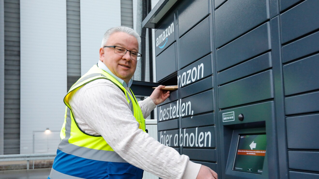 Ein Mann in Sicherheitsweste vor einem Amazon Locker