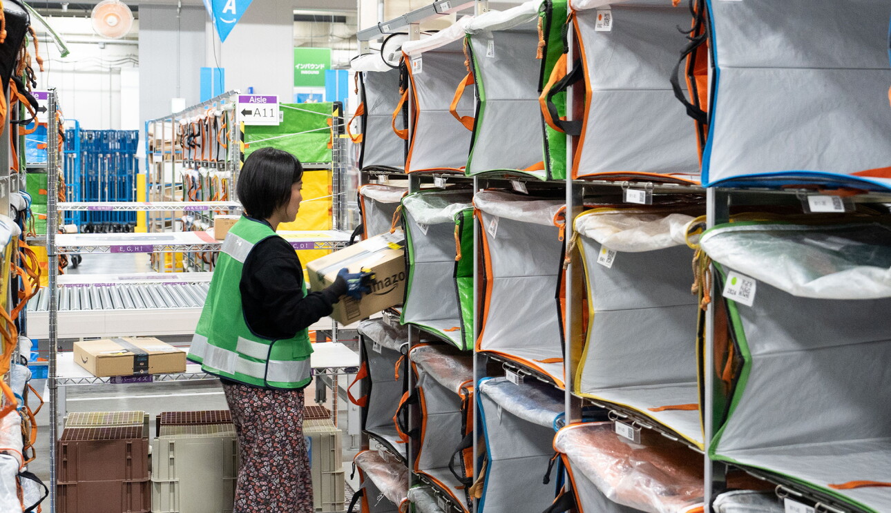 箱型の入れ物に商品の入った段ボール箱を入れている女性