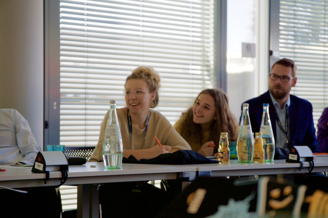 Links im Bild: die Teilnehmerinnen von Jugend gründet. Rechts ist ein Herr im blauen Anzug zu sehen. Alles sitzen an einem Konferenztisch. Im Vordergrund sind Getränke auf dem Konferenztisch.