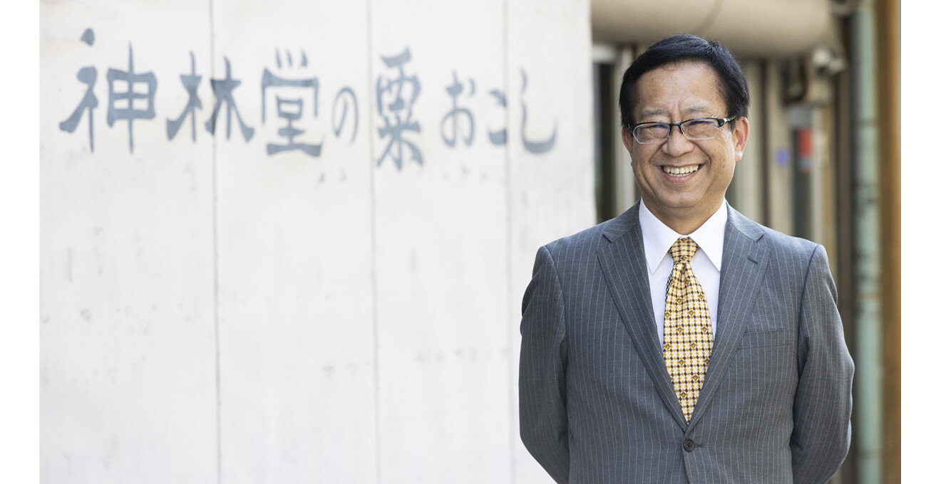 『神林堂の粟おこし』の文字を背景に笑顔の岸本さんの写真