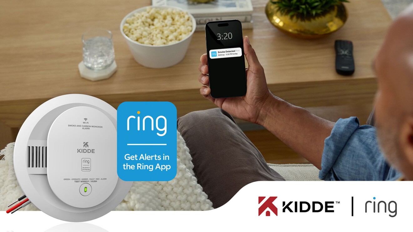 A person viewing a Ring notification of smoke detected on their mobile device. A Kidde smoke alarm is also visible.