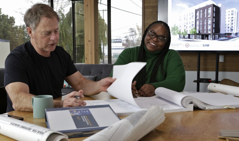 A photo of two people sitting at a desk reviewing blueprints. 