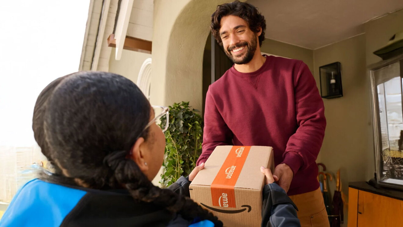 家の外で配達員から段ボール箱を受け取る笑顔の男性。段ボール箱はAmazonロゴ入りのテープで閉じられている。