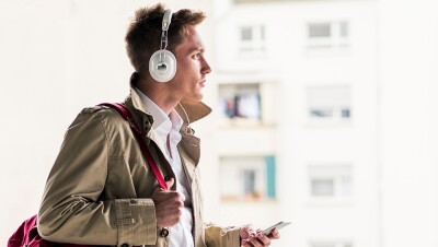 A stylishly dressed man listens to audio from his smartphone via headphones