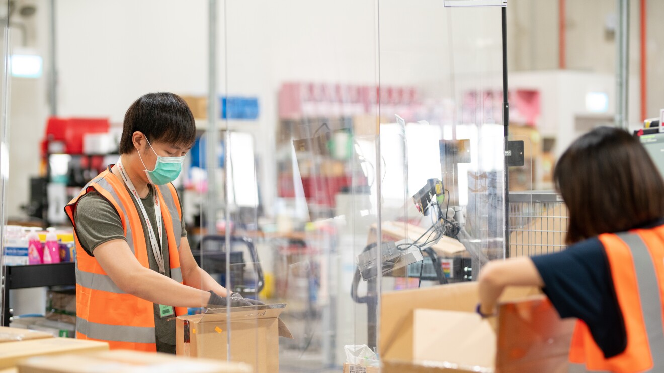 Two people can be seen working on an Amazon package with a glass barrier between them