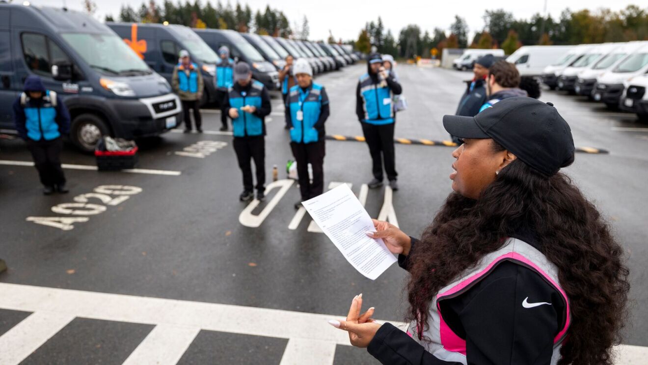 Woman with clipboard addresses group of uniformed employees in parking lot