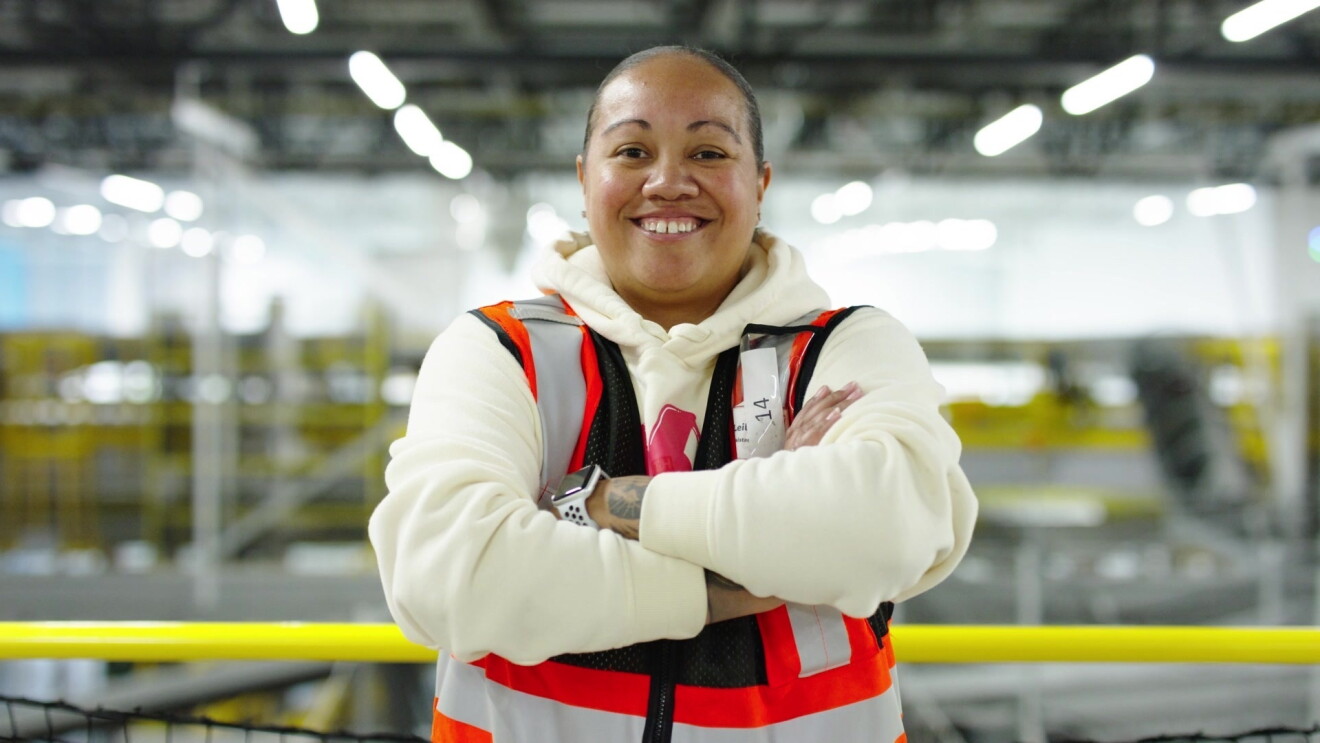 Amazon employee Leilani smiles with her arms crossed while she works at the fulfillment center she manages.