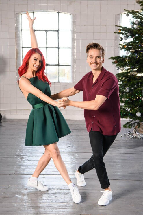 Dianne Buswell and  Joe Sugg dancing in a studio, behind them is a Christmas tree.