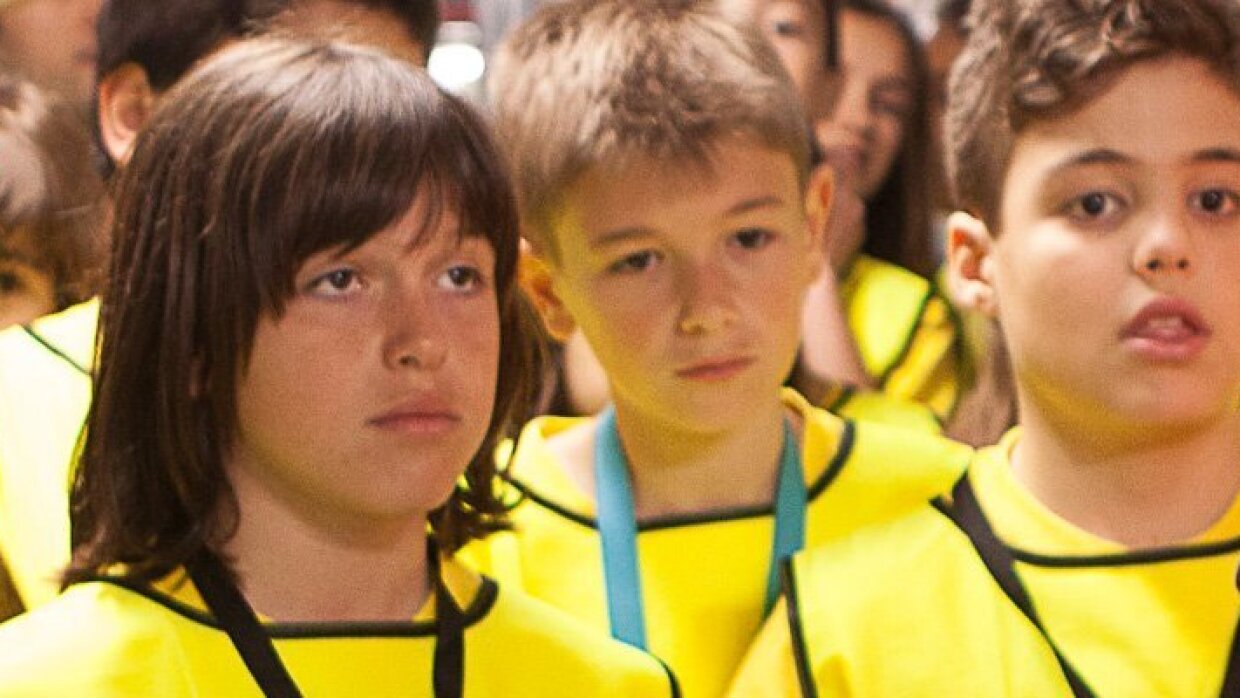 Seis estudiantes de primaria, en primer plano, con sus chalecos amarillos escuchan atentamente las explicaciones de su guía durante el tour por el centro logístico.