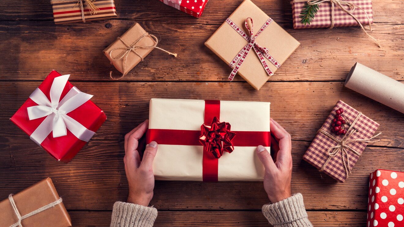 A flatlay of a pair of hands holding a wrapped gift, with other wrapped gifts scattered around the table.