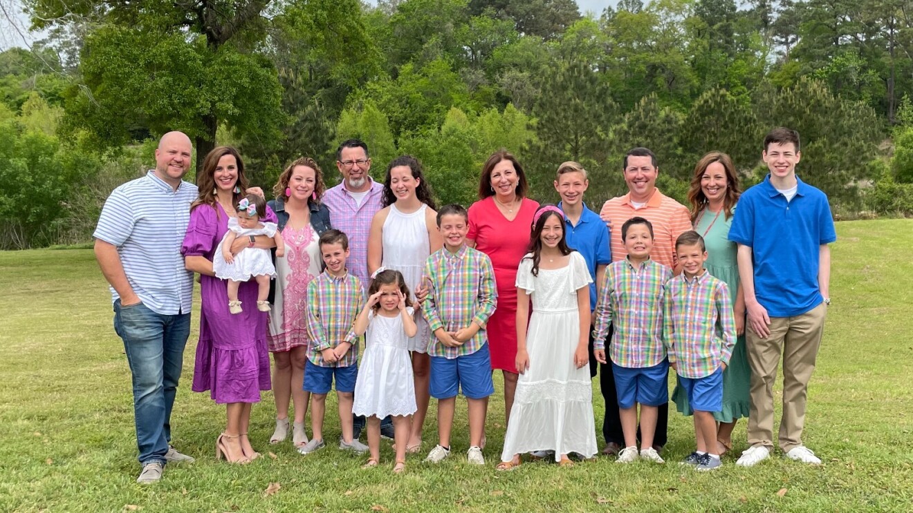 Rebecca is surrounded by her children and grandchildren outside as they all pose and smile for a family photo.