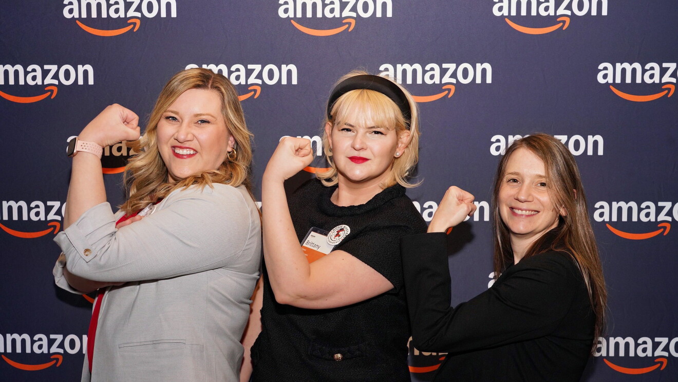Three women posing confidently with raised fists at Amazon event