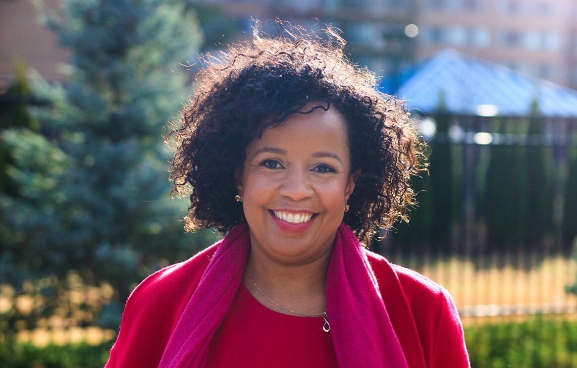 An image of a woman smiling for a photo while standing outside in front of an apartment building. 