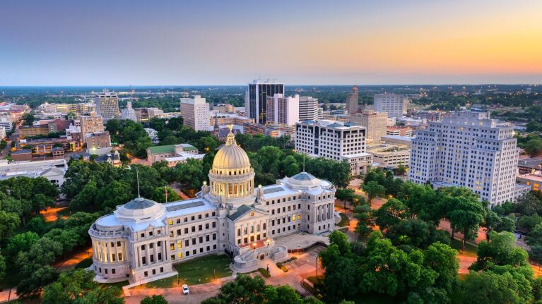Aerial view of Mississippi State Capitol building with golden dome surrounded by trees at sunset