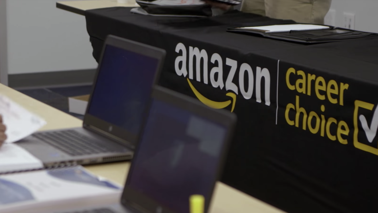 Two notebook computers sit on a table top, in front of them in a table with a drape that says "Amazon Career Choice"