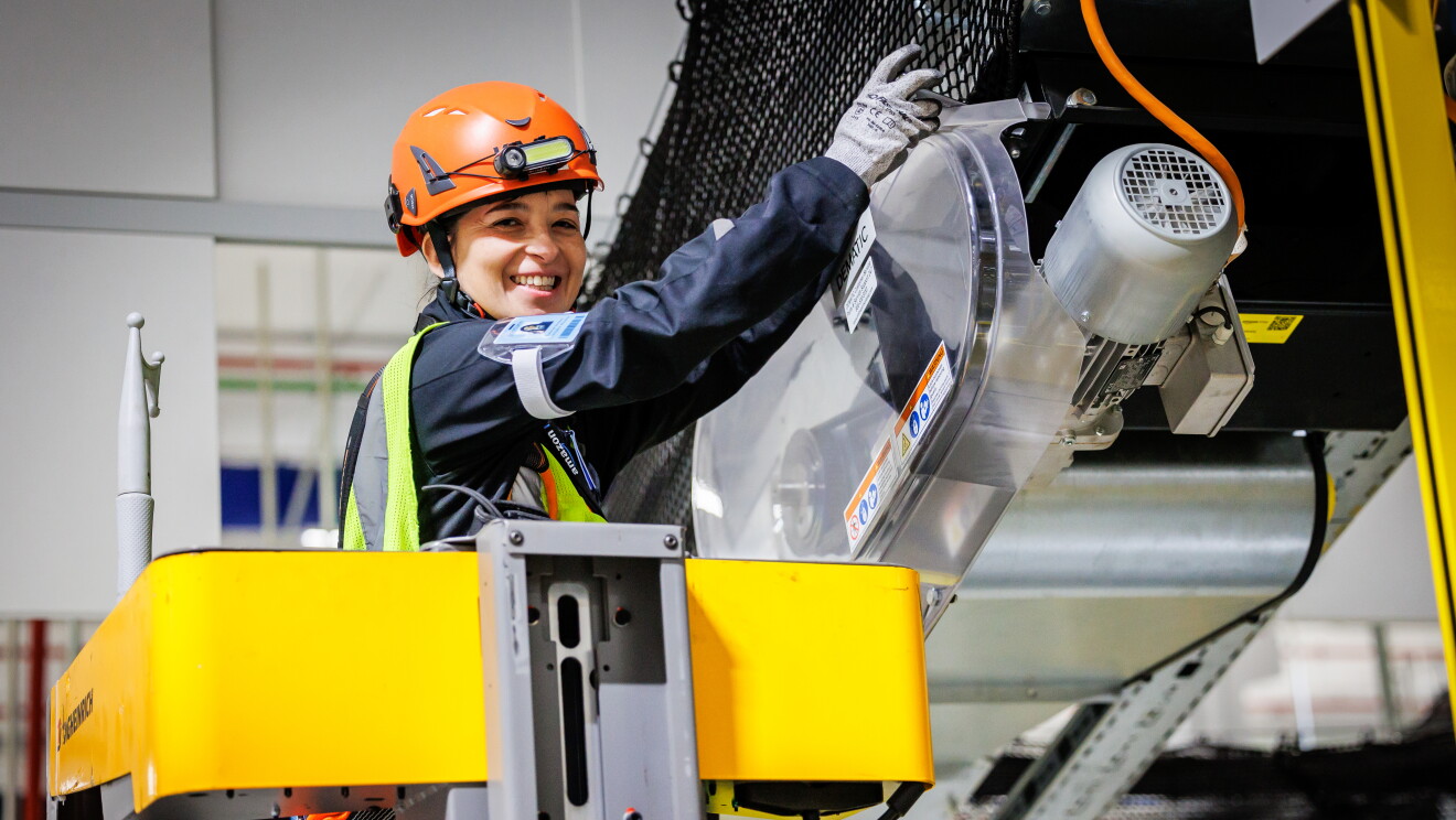 Mujer trabajando arreglando una máquina dentro de un centro logístico. 