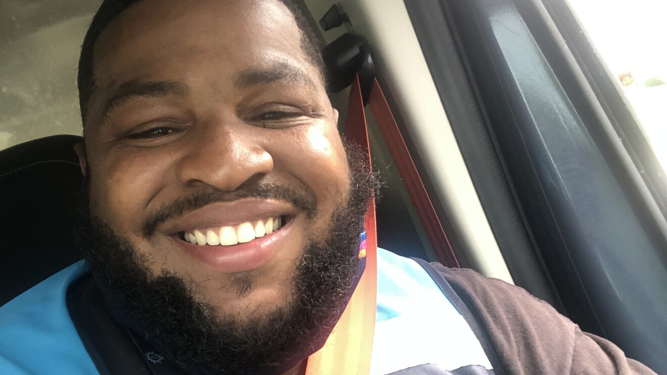 An image of a man smiling for a selfie in his car. He is wearing the blue Amazon delivery vest.
