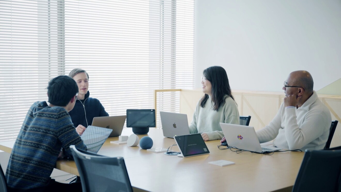 会議室で話し合っている女性1人と男性3人。机の真ん中にAmazon Echoが置かれている