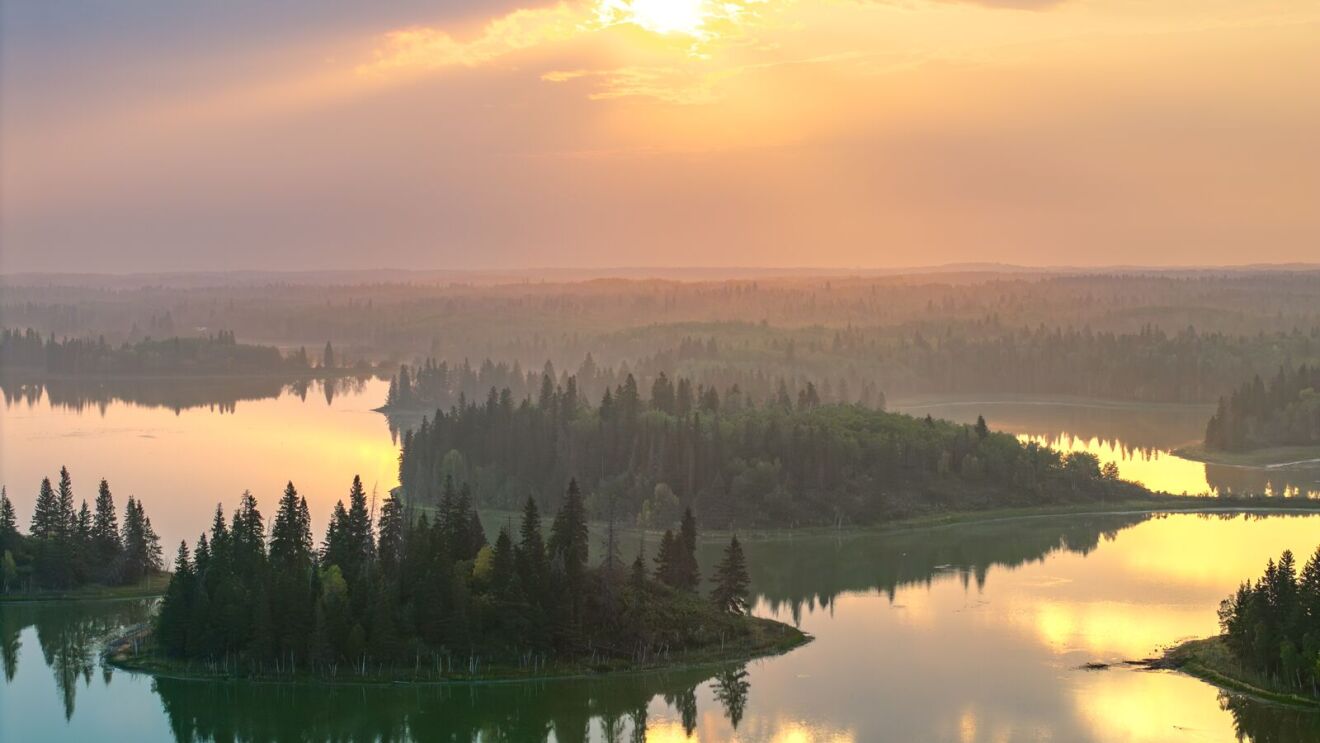 Misty forested islands surrounded by calm water reflecting golden sunset light