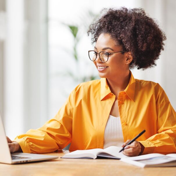 woman with glasses smiling while working on her laptop