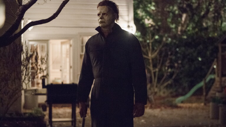 Menacing figure in dark clothing standing in shadowy yard at night