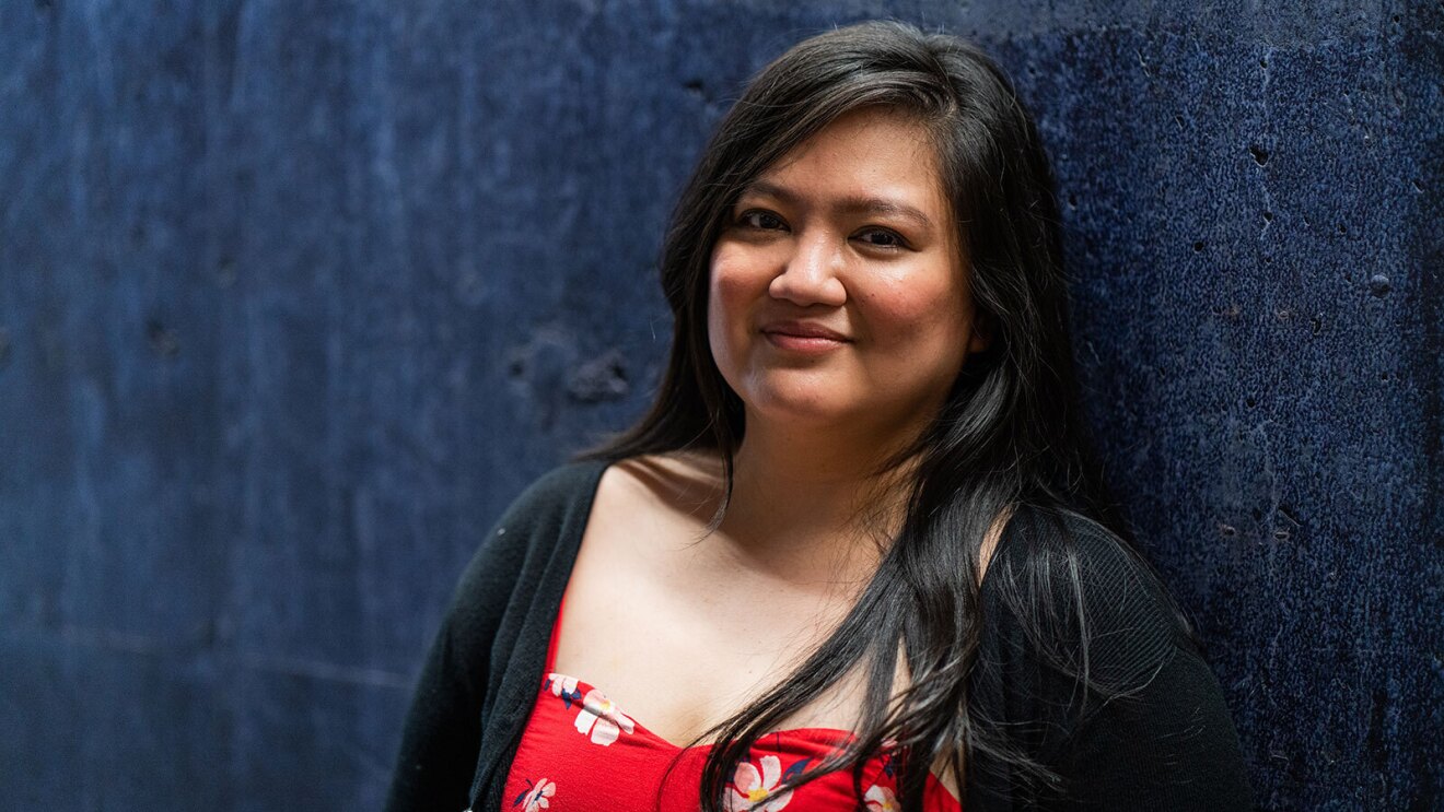 A headshot image of a woman smiling for a photo in front of a dark blue wall.
