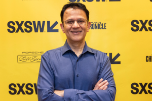 A photo of Vishal Sharma, Vice President, Artificial General Intelligence, standing with his arms crossed in front of a SXSW 2024 backdrop.