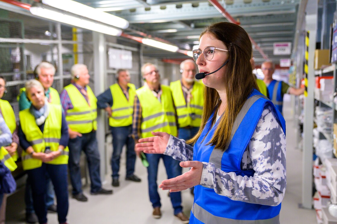 Eine Frau in blauer Sicherheitsweste vor einer Besuchergruppe