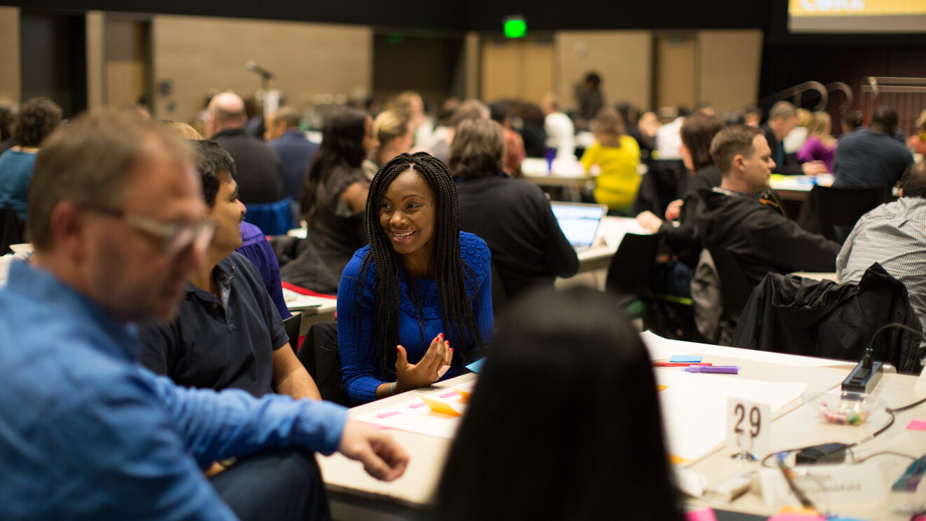 Men and women gather together at tables in a conference setting